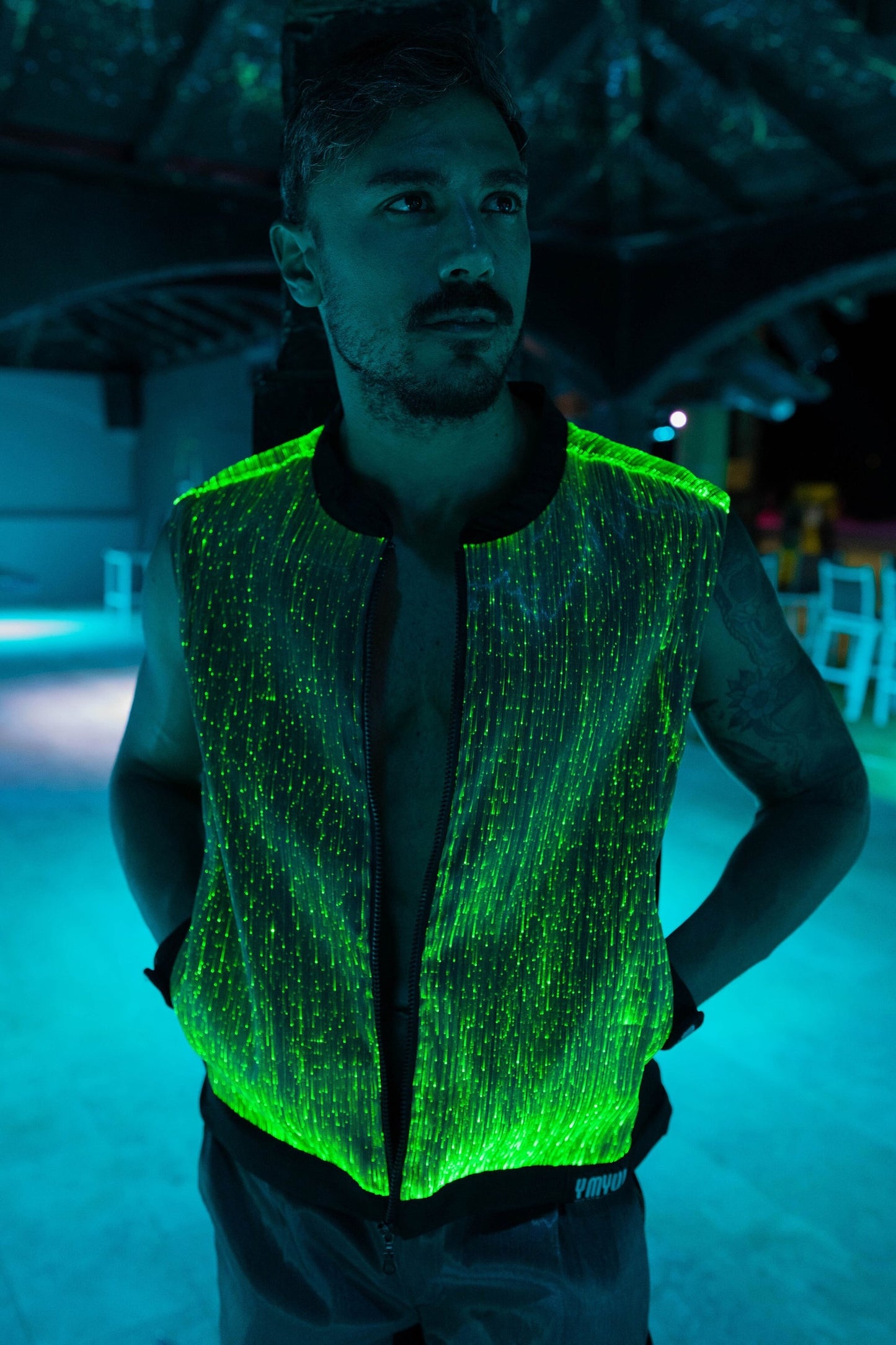 Man wearing a black fiber optic light up vest illuminated in green light against a dark background