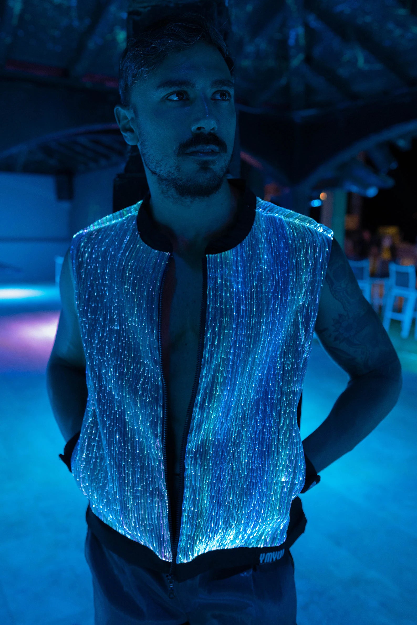 Man wearing a black fiber optic light up vest illuminated in light blue against a dark background