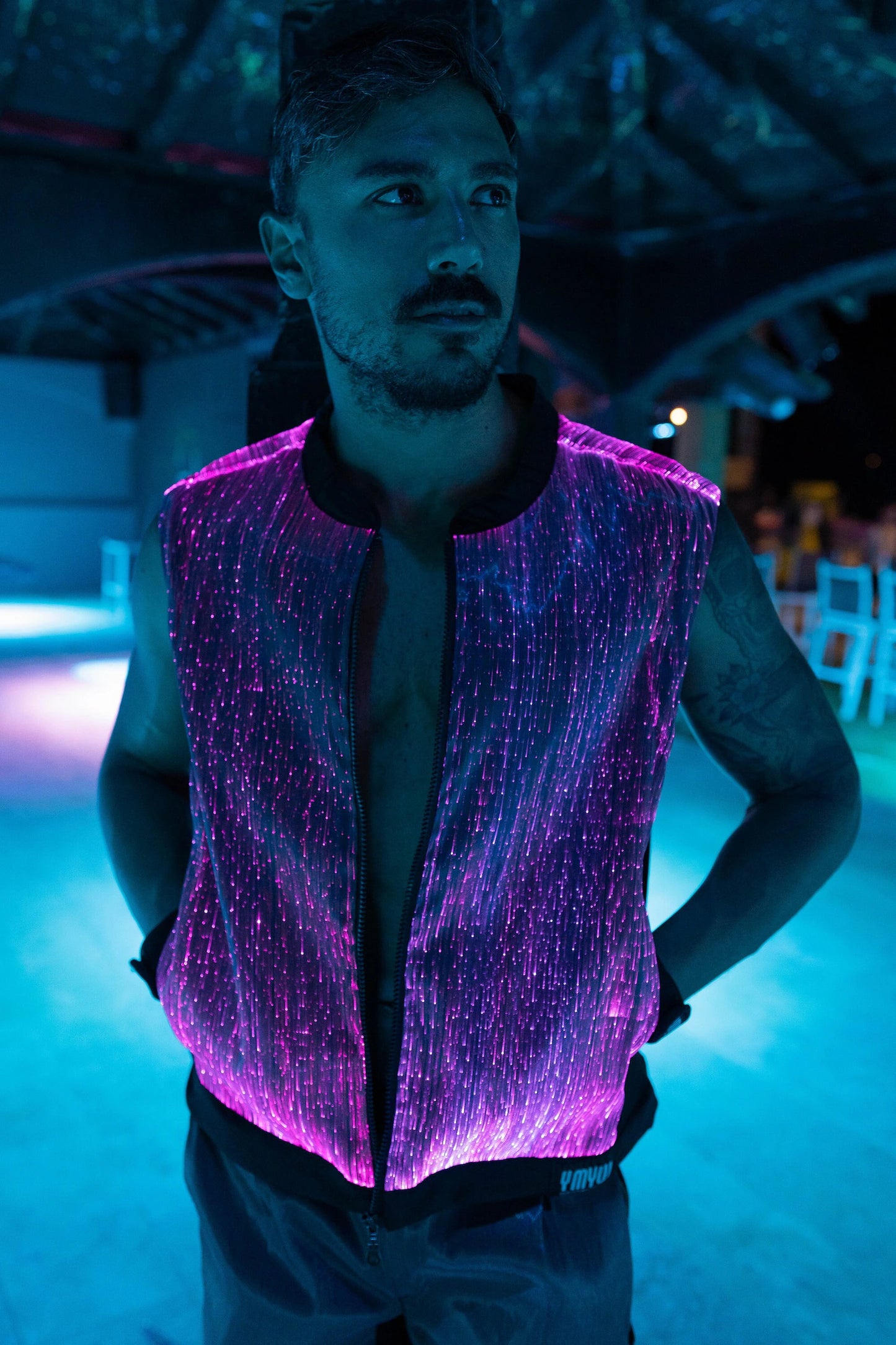 Man wearing a black fiber optic light up vest illuminated in purple light against a dark background